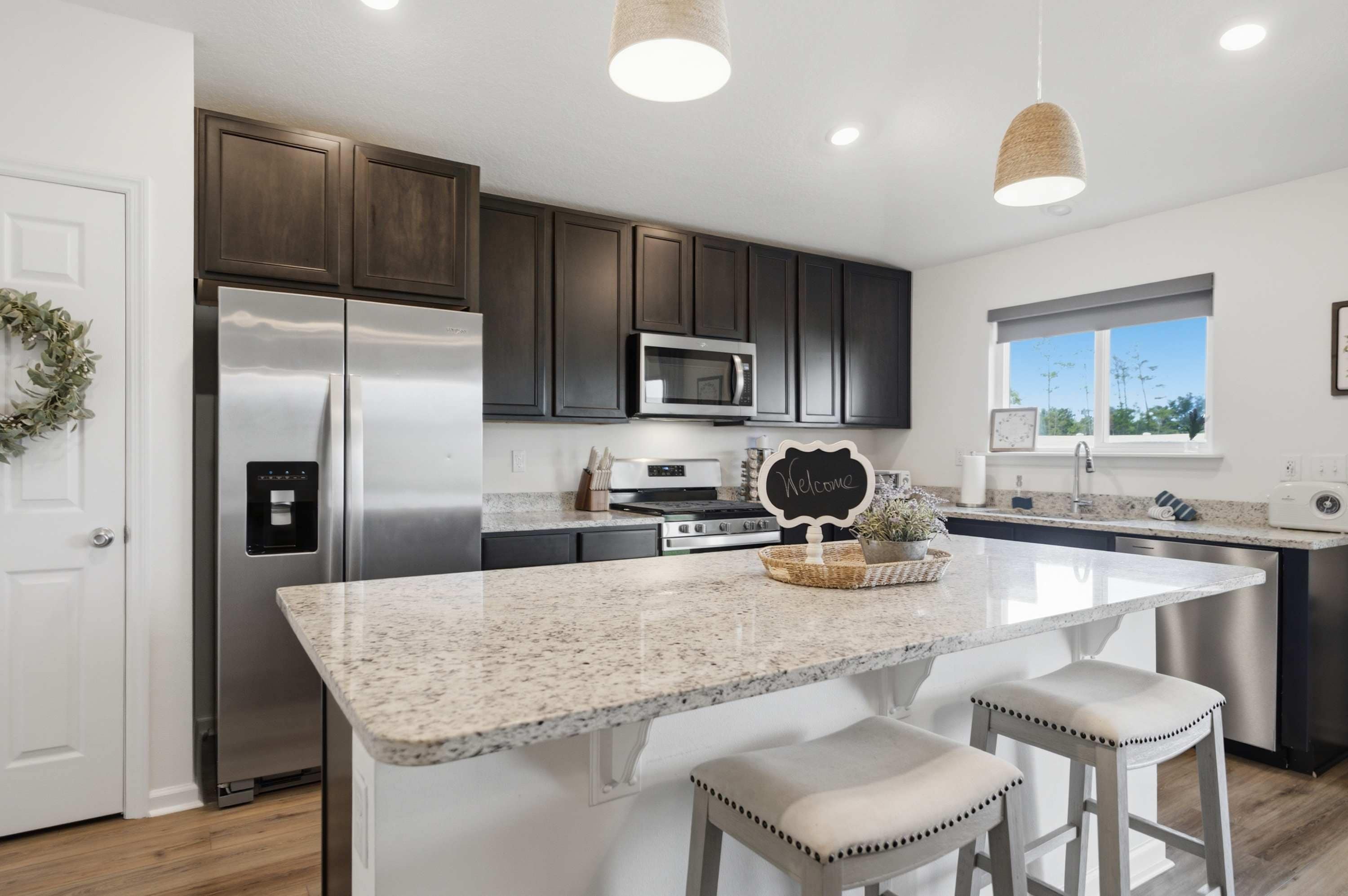 A modern kitchen with dark cabinets, stainless steel appliances, a granite countertop, and a welcome sign.