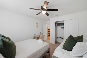 Ein Schlafzimmer mit zwei Betten, einem Deckenventilator, einem Schreibtisch und einem Stuhl.