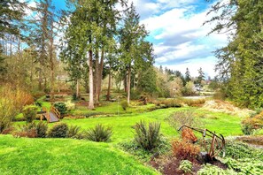 A lush garden with a wooden bridge, surrounded by tall trees and a variety of plants.