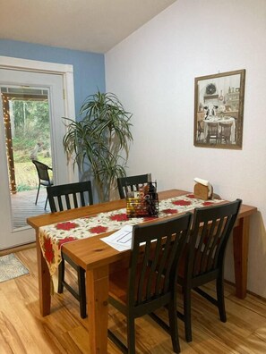 A dining area with a wooden table, four chairs, a potted plant, and a framed picture on the wall.