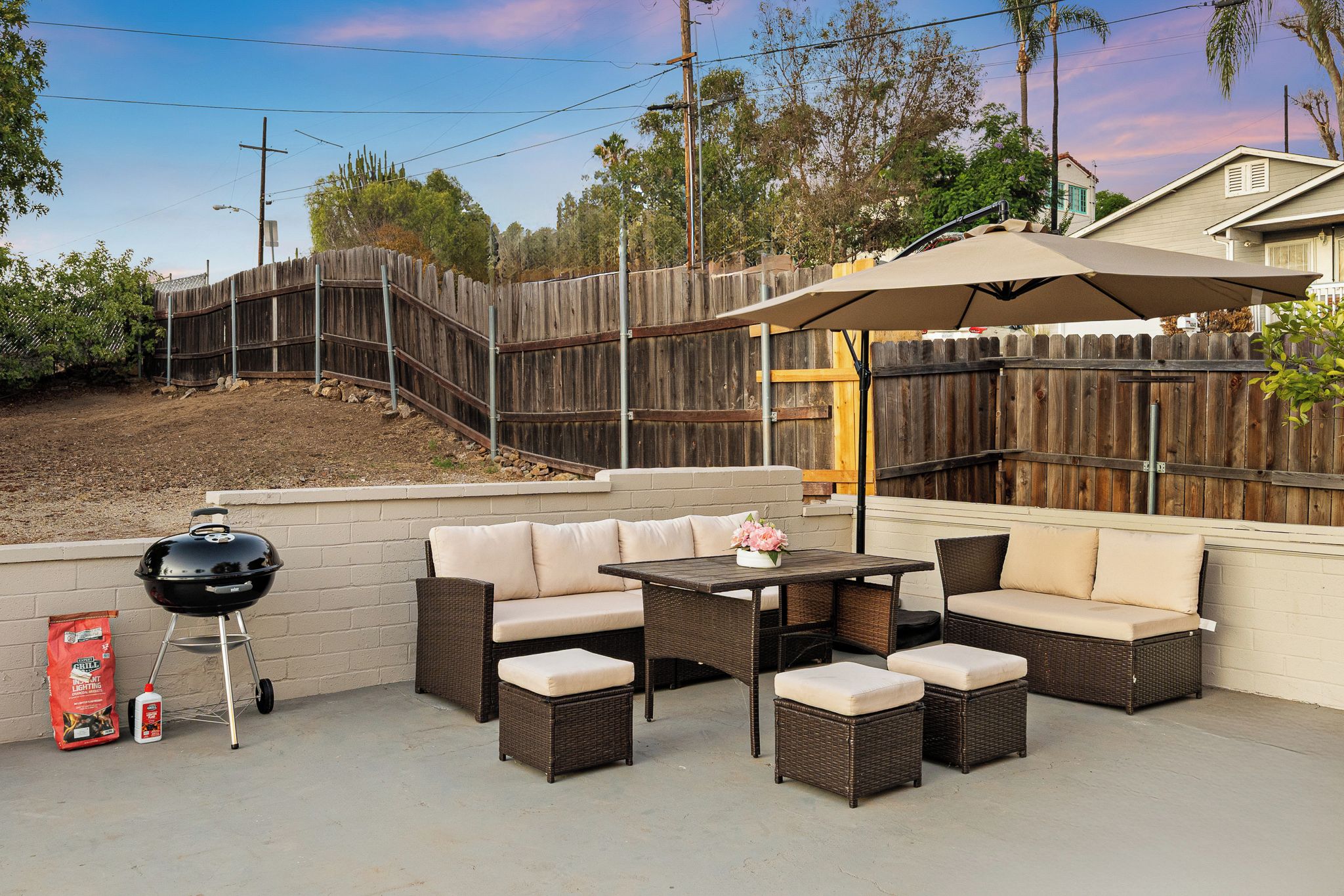 An outdoor patio with wicker furniture, a grill, and a wooden fence.
