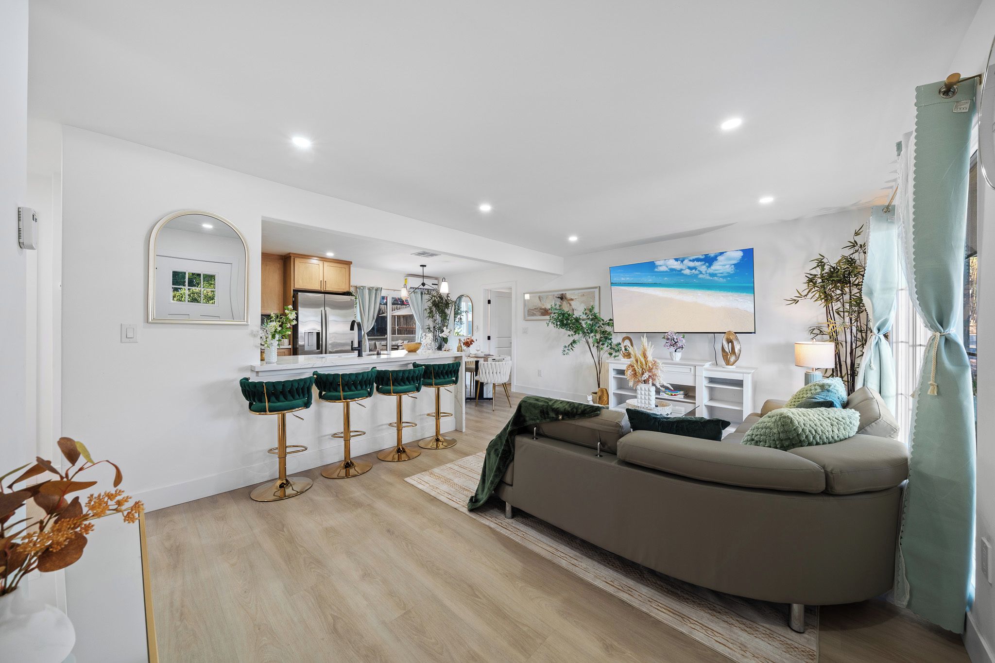 Una sala de estar moderna con un sofá, un comedor con taburetes de bar, una cocina con refrigerador y un televisor montado en la pared.