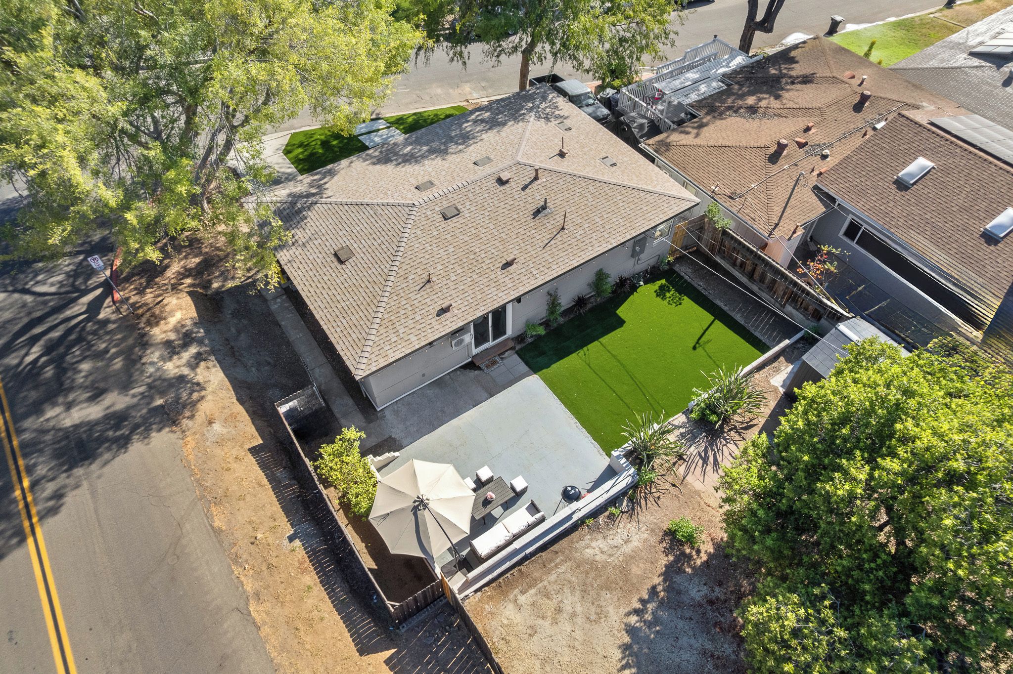 A residential property with a paved driveway, a green lawn, and a covered outdoor seating area.