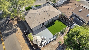 A residential property with a paved driveway, a green lawn, and a covered outdoor seating area.