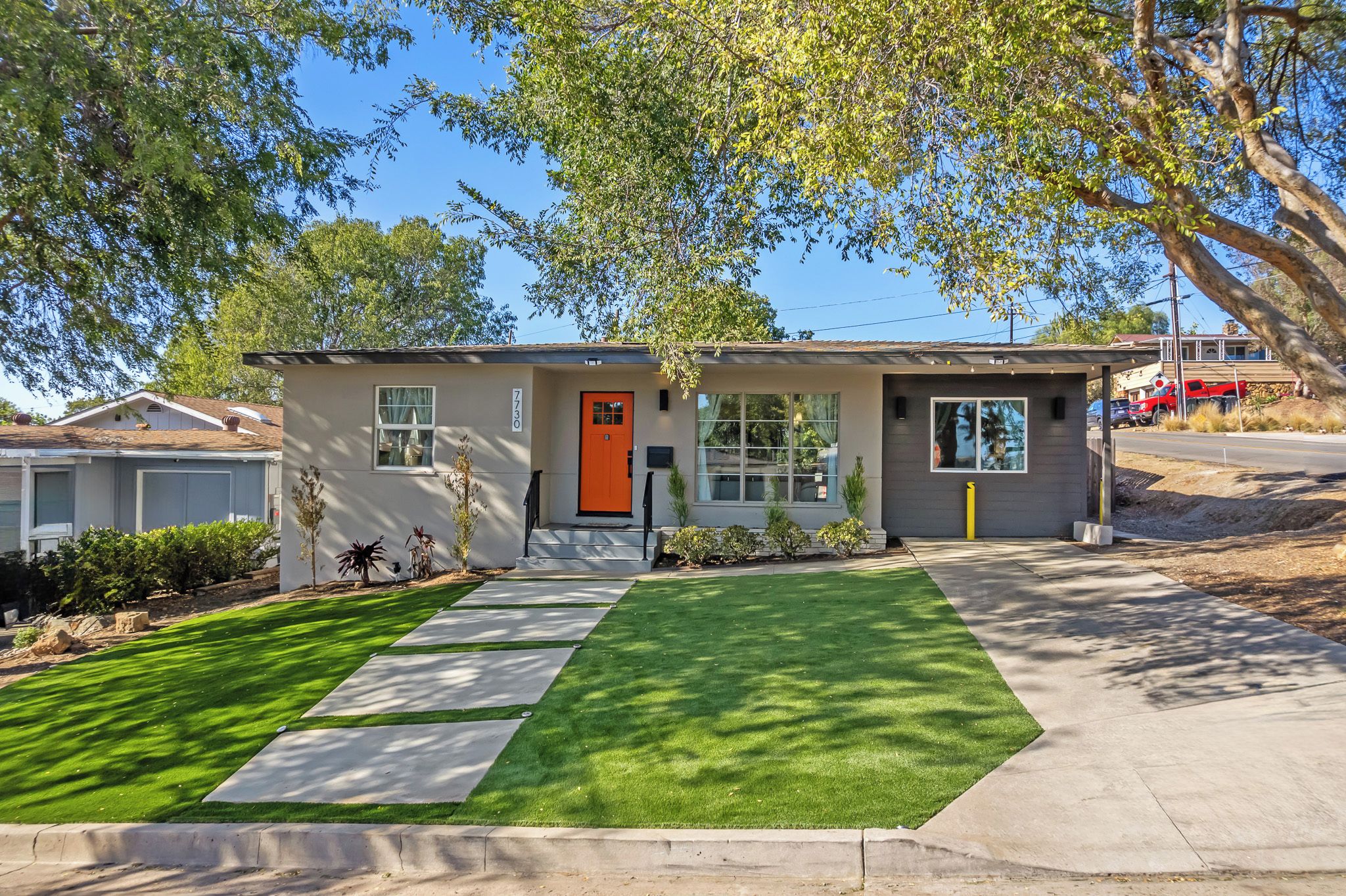 A single-story house with a well-maintained lawn, a clear driveway, and a distinct orange door.