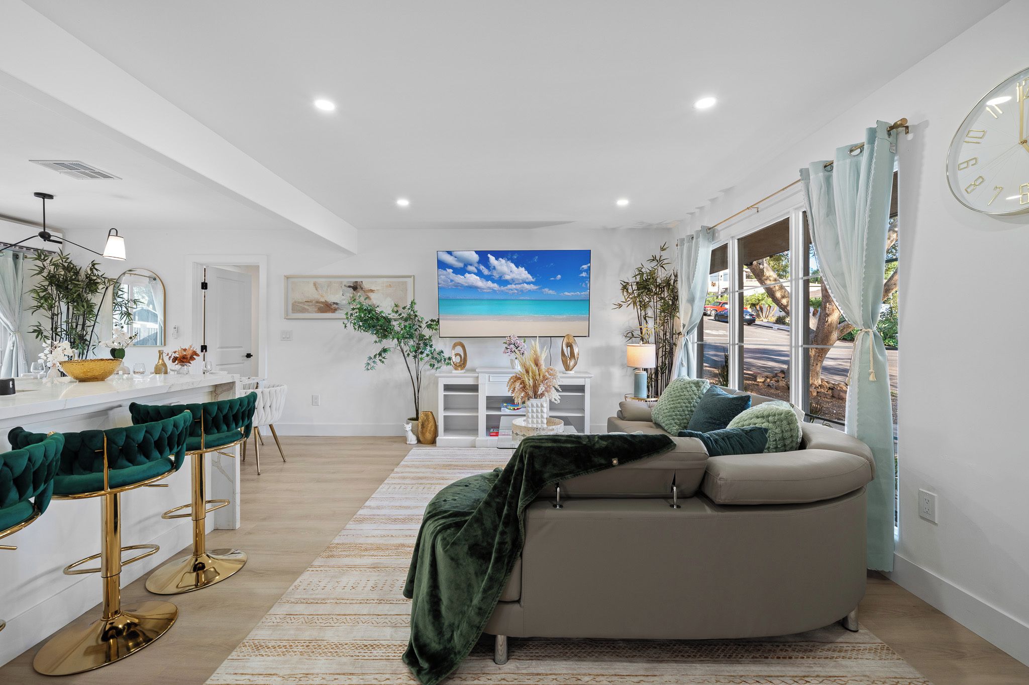 A modern living room with a sofa, a dining area with bar stools, and a large TV displaying a beach scene.