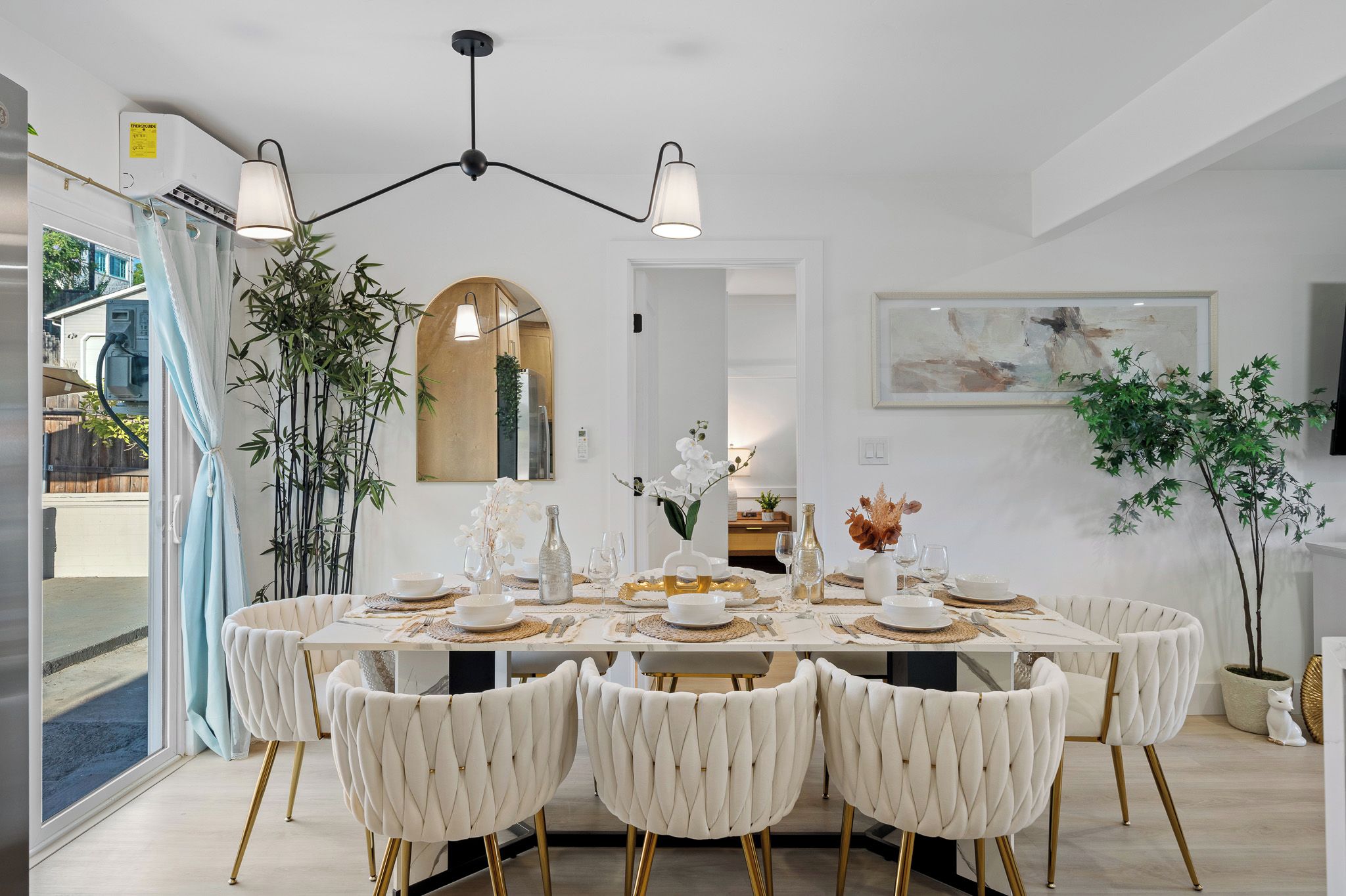 Un comedor con una mesa blanca dispuesta para seis personas, rodeada de sillas capitonadas con patas doradas.