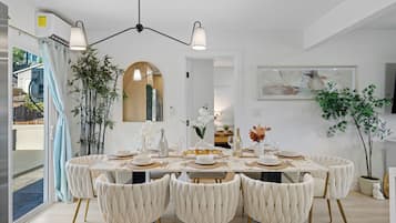 Un comedor con una mesa blanca dispuesta para seis personas, rodeada de sillas capitonadas con patas doradas.