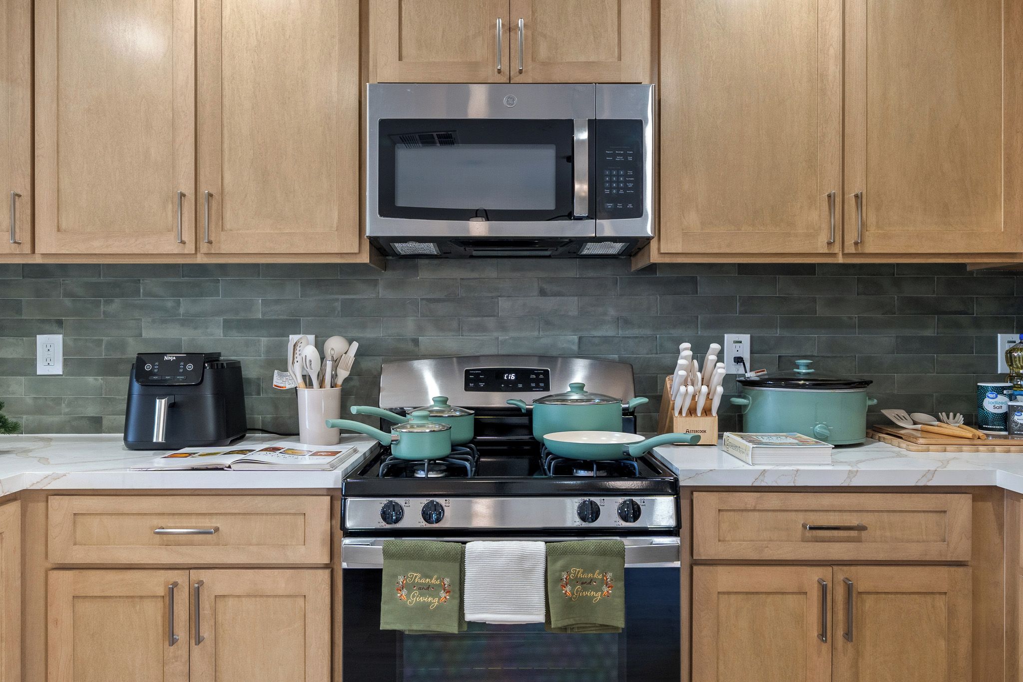 A kitchen with wooden cabinets, a stainless steel microwave, a stove with pots, a coffee maker, and a knife block.