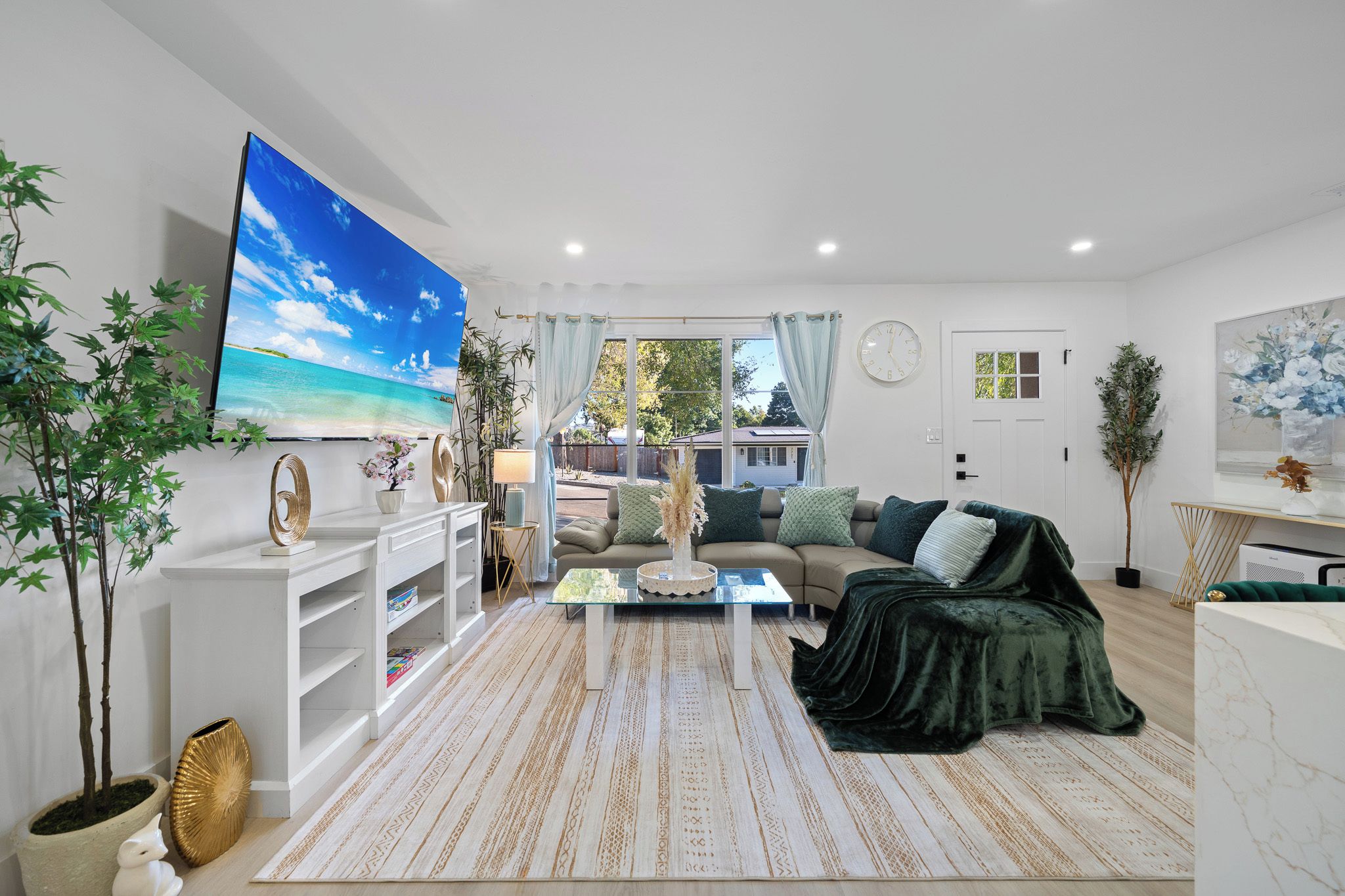 A living room with a large flat-screen TV, a sofa, a coffee table, and a patterned rug.