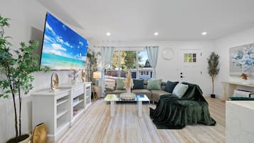 A living room with a large flat-screen TV, a sofa, a coffee table, and a patterned rug.