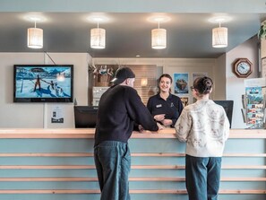 A reception area with a flat-screen TV displaying a video game, a reception desk, and a clock on the wall. - Belambra Club Orcieres 1850 Le Roc Blanc - Winter & Summer (Orcieres)