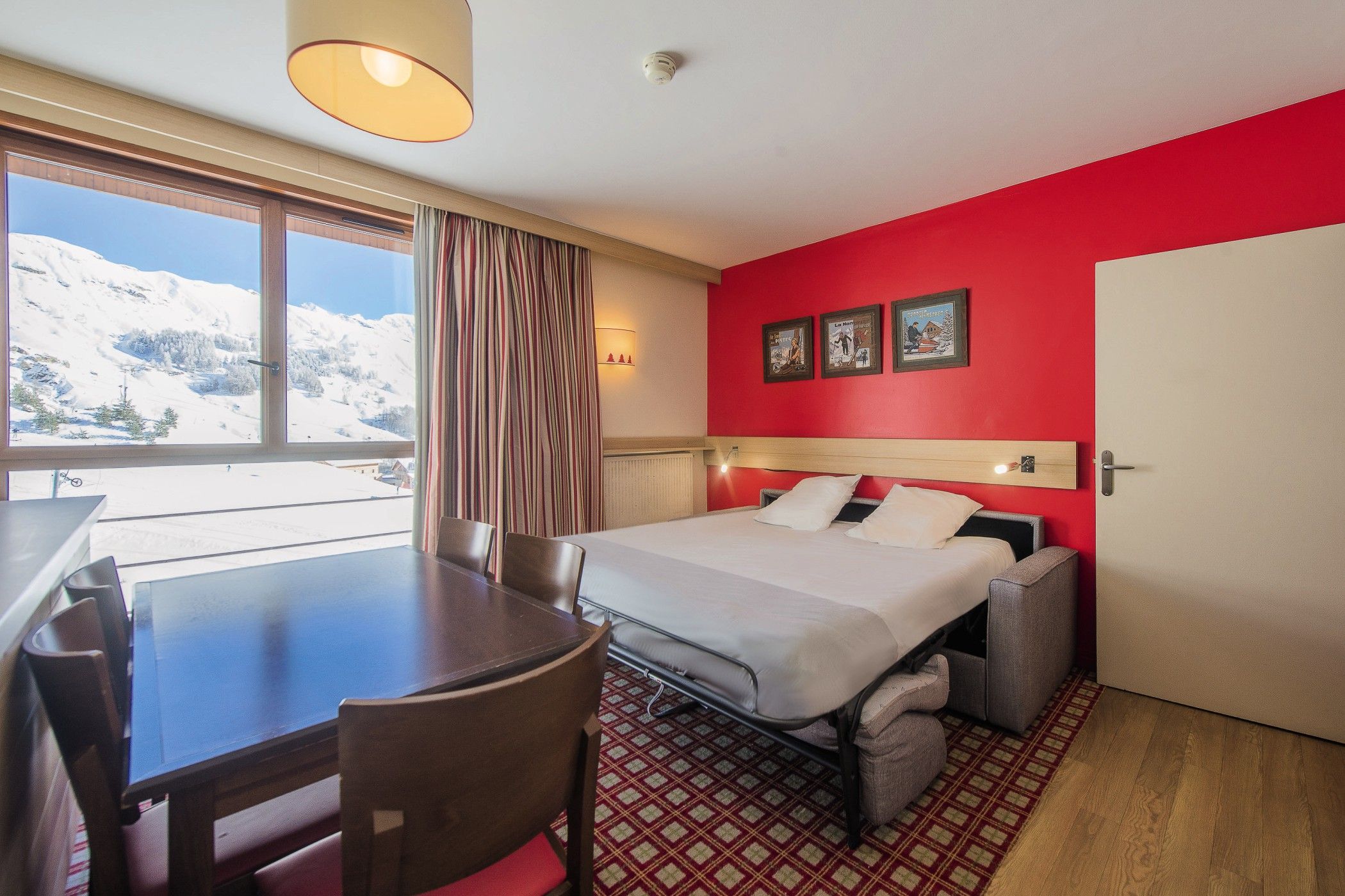 A hotel room with a bed, a desk, and a view of a snowy mountain.