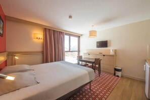 Une chambre d’hôtel équipée d’un lit, d’un bureau, d’une chaise, d’une télévision et d ’une fenêtre avec des rideaux.