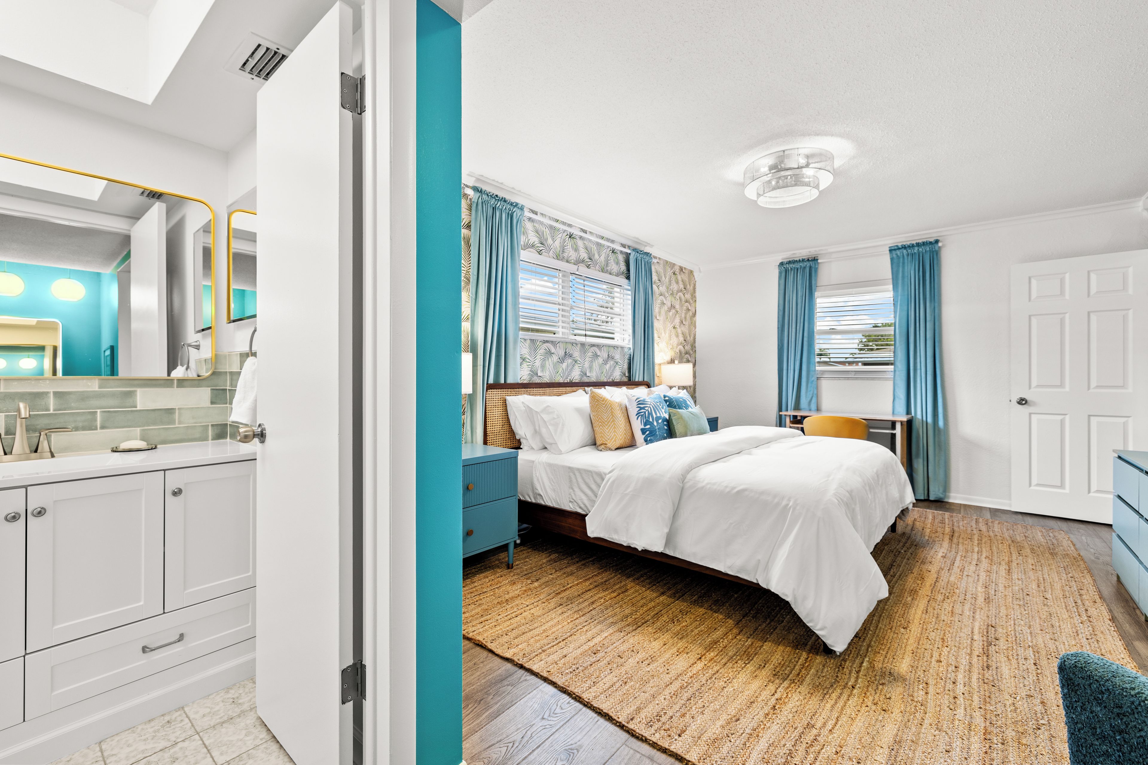 Une chambre moderne comprenant un lit, des tables de chevet, un miroir et une salle de bain avec un lavabo et des toilettes.