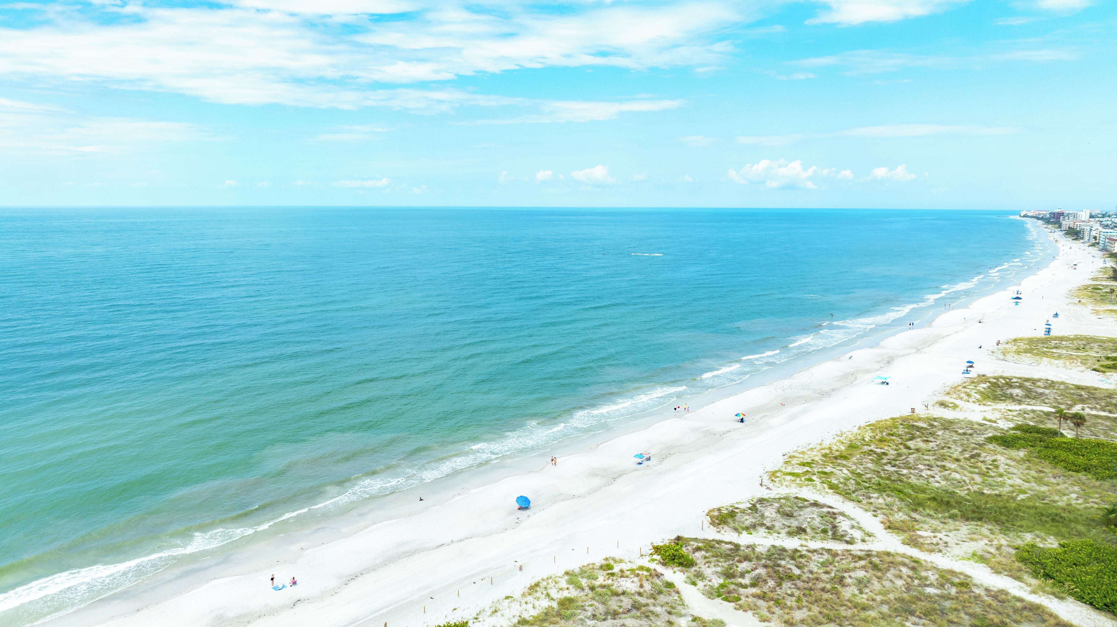 A beach with a long stretch of white sand, clear blue water, and a few umbrellas.