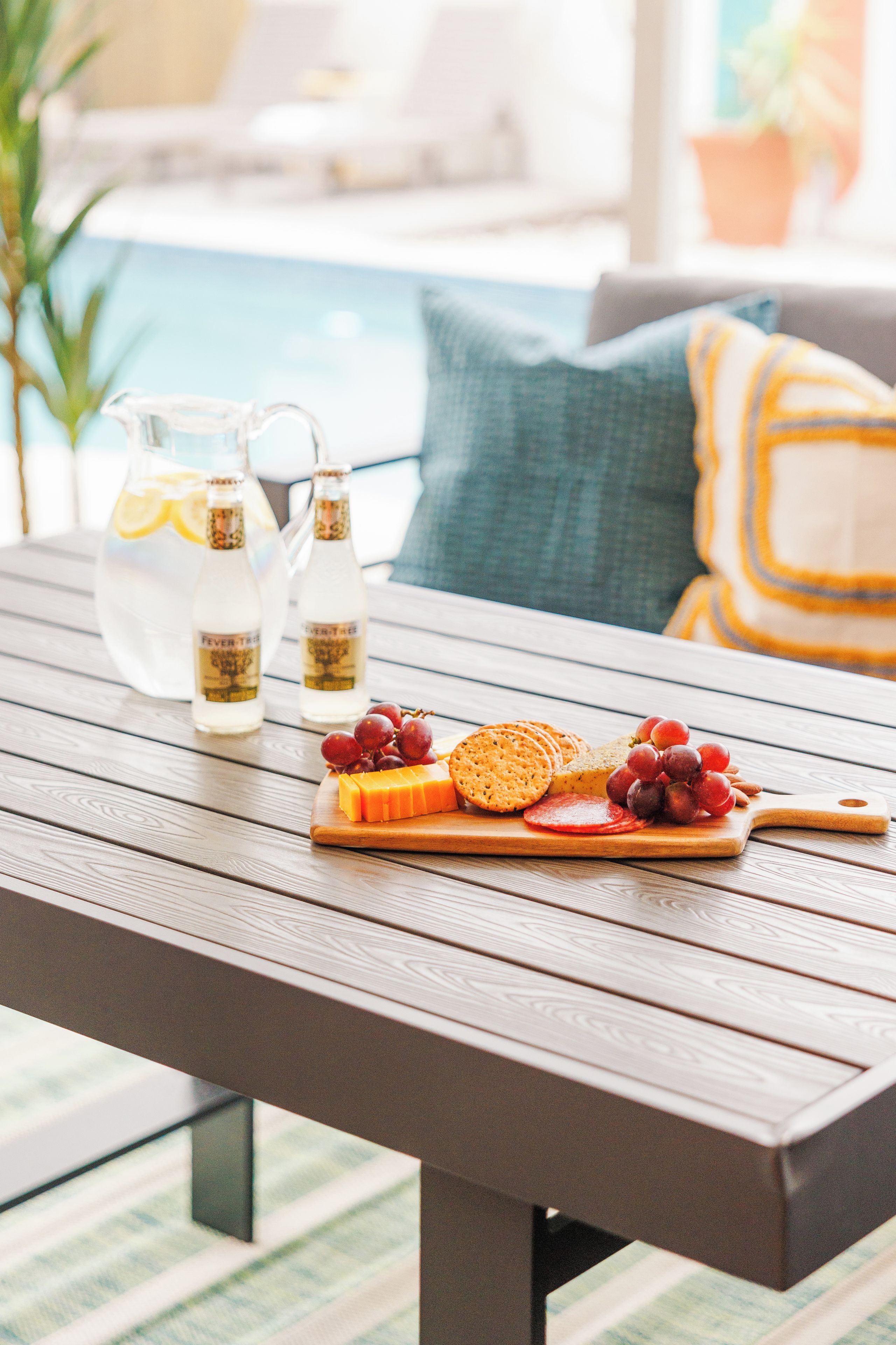 A wooden table with a cheese board, crackers, grapes, and a pitcher of water.