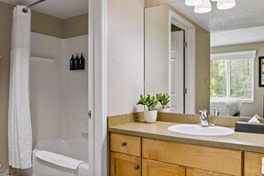 Une salle de bain avec une douche, un lavabo, un miroir et une plante en pot.