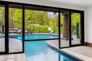 Une piscine donnant sur une forêt, avec de grandes portes vitrées.