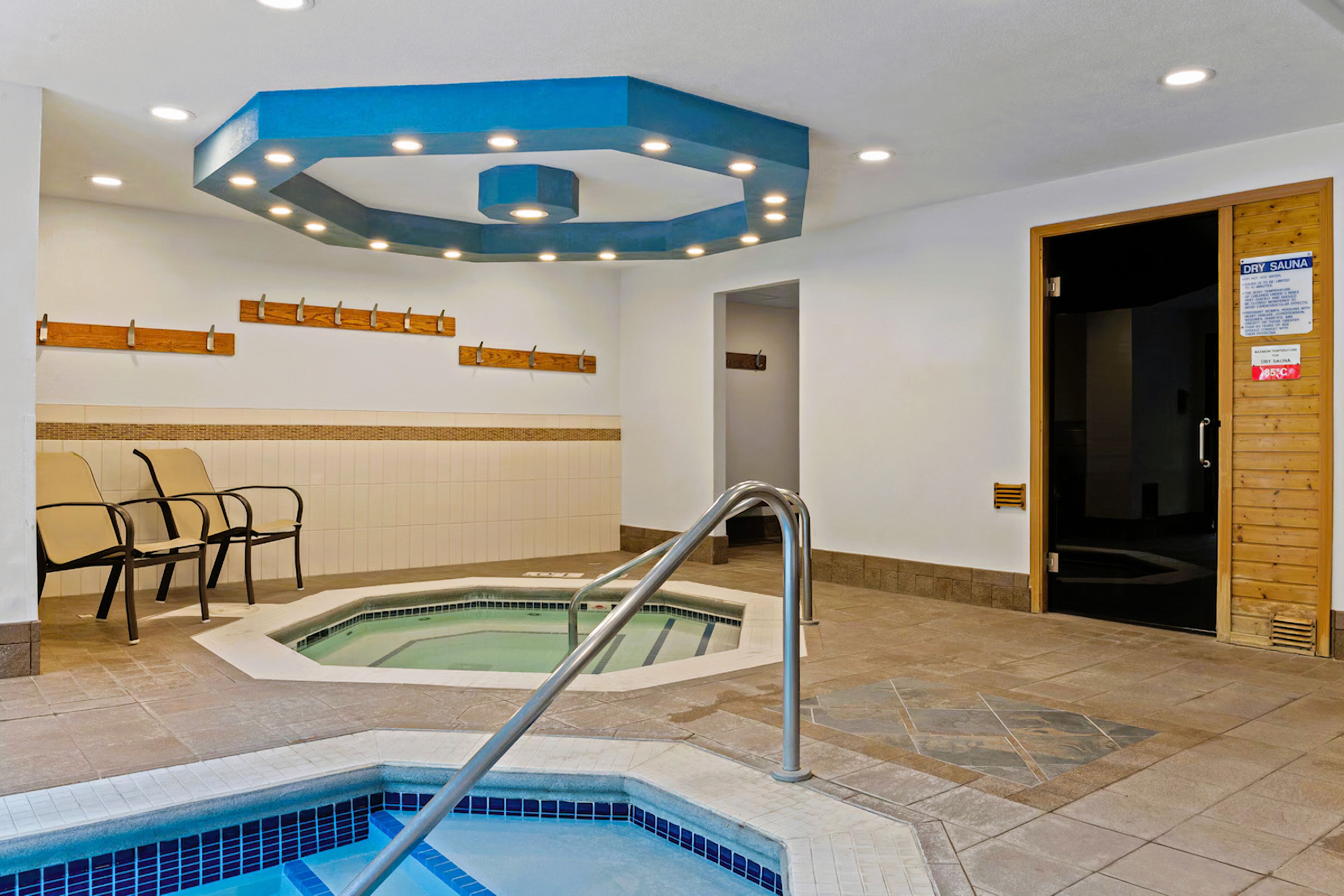 Un sauna seco con piso de baldosas, una piscina y una puerta de madera.