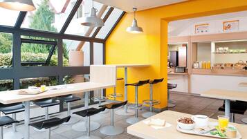 Un café moderne avec des tables hautes, des tabourets de bar et des luminaires suspendus.