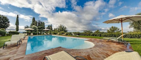 Una piscina con sillas de descanso y sombrillas, rodeada de vegetación y árboles.