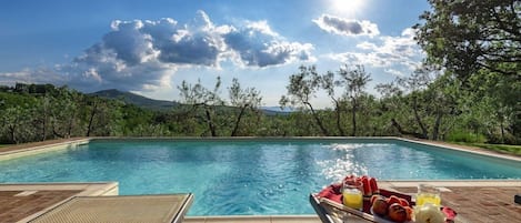 Une piscine avec un plateau de petit-déjeuner posé sur le bord, entourée de verdure et sous un ciel dégagé.