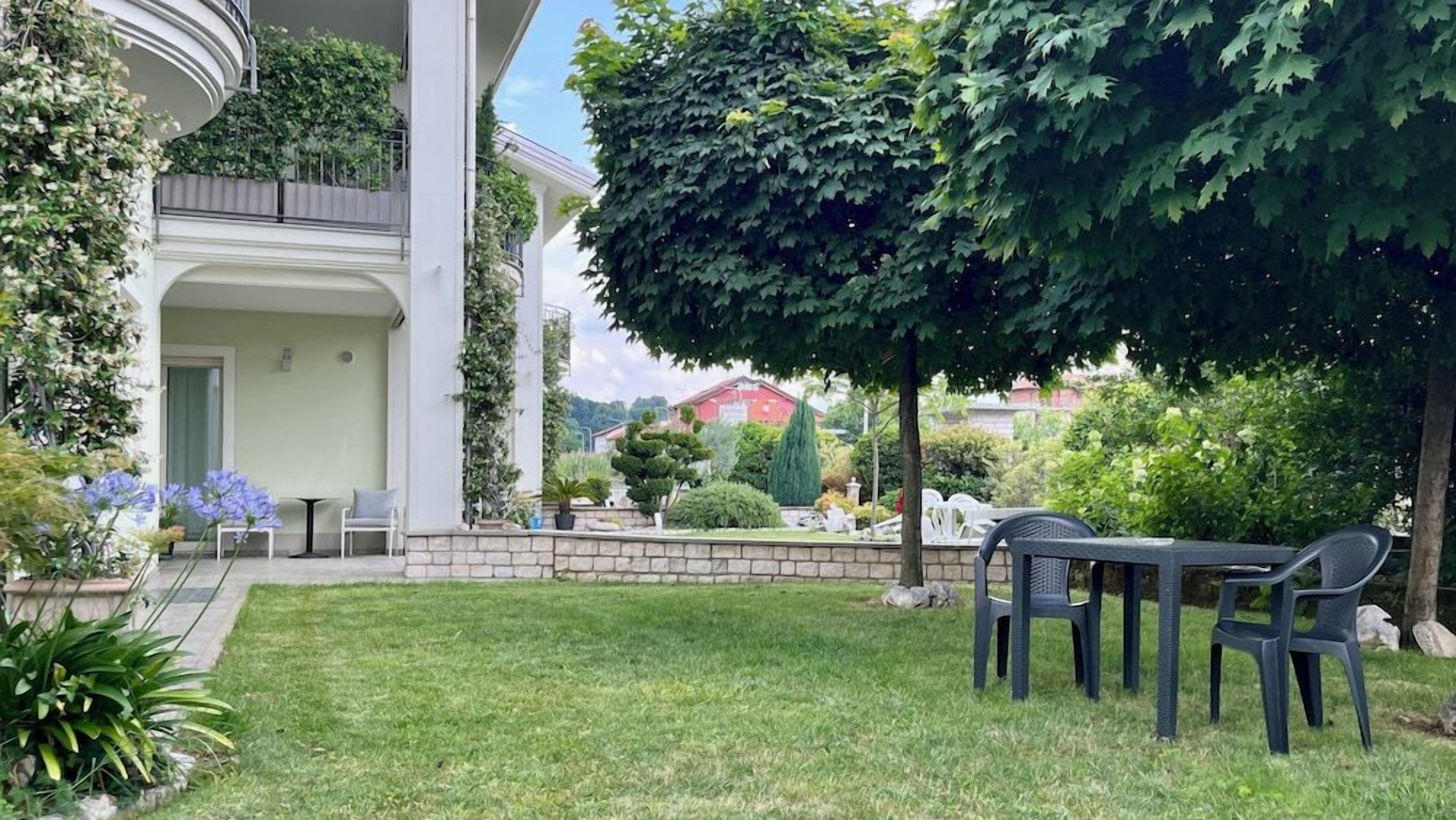 Ein Wohnhaus mit gepflegtem Rasen, einer Sitzgelegenheit im Freien und einem großen Baum, der Schatten spendet.