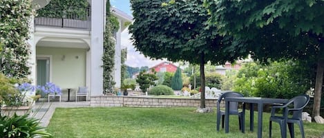 Propiedad residencial con césped cuidado, zona de estar al aire libre y un gran árbol que proporciona sombra.
