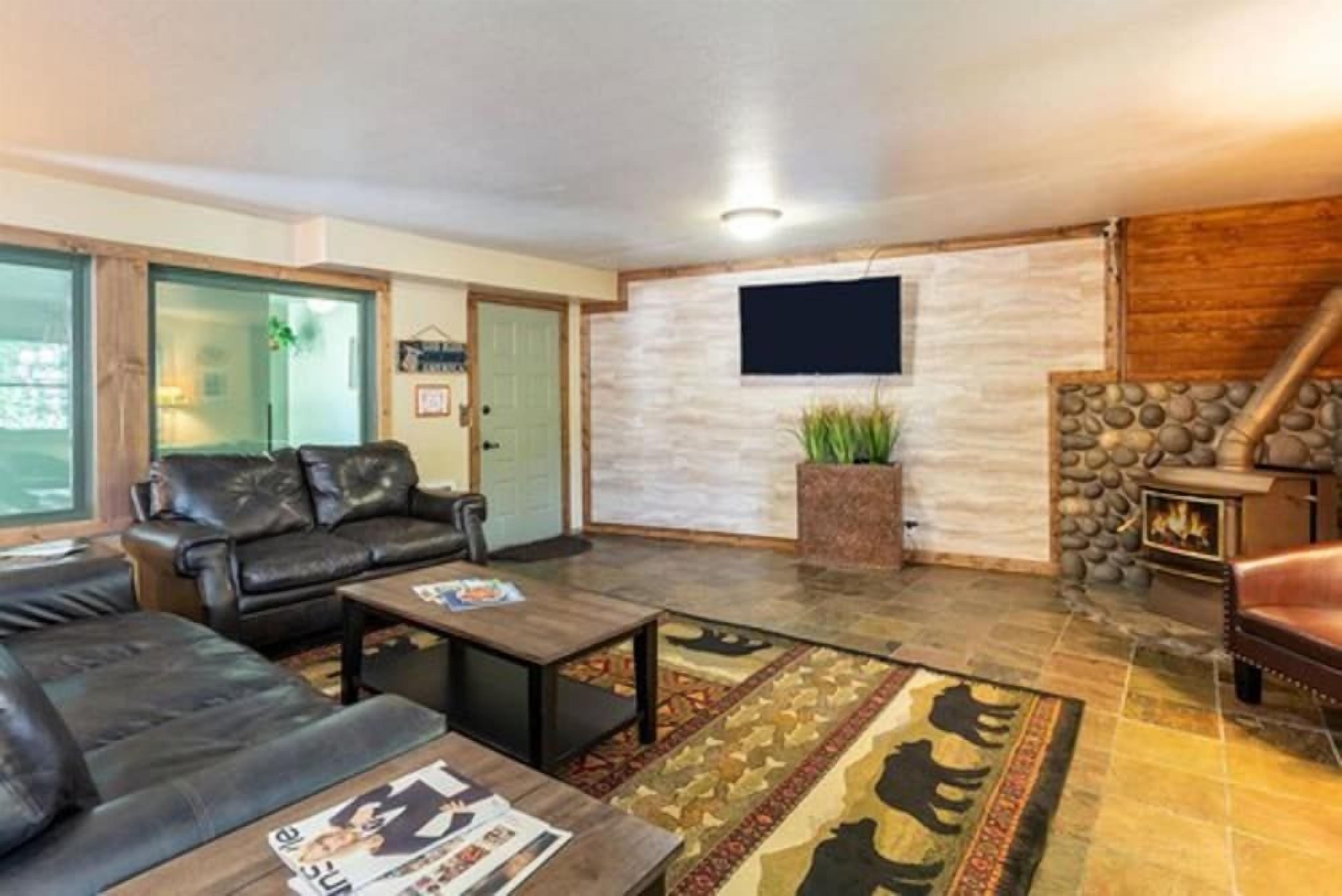 A living room with a stone fireplace, leather sofas, a flat-screen TV, and a patterned rug.