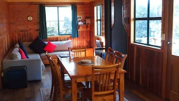 A cozy cabin interior with a dining table, chairs, a sofa, and a large window.