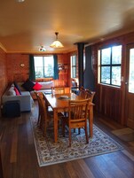 Interior acogedor de una cabaña con una mesa de comedor, sillas, un sofá y un ventanal grande.