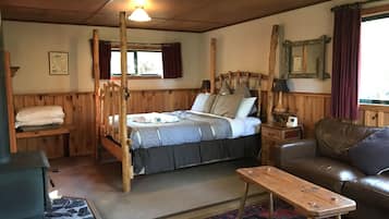 A wooden four-poster bed with a blue and gray bedspread, a wooden bench, a leather sofa, and a patterned rug.