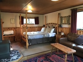 Una habitación acogedora con una cama de madera con dosel, un sofá de cuero marrón, una pequeña mesa de madera y una alfombra estampada.
