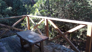 A wooden deck with a table and railing, surrounded by dense foliage.