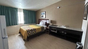 Una habitación de hotel con cama, escritorio, lavabo y ventana con cortinas.
