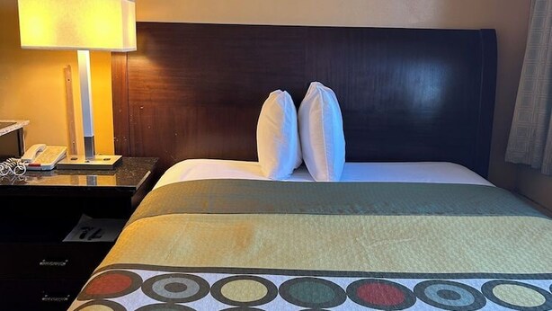 Una habitación de hotel con una cama, una mesita de noche con lámpara y un teléfono.