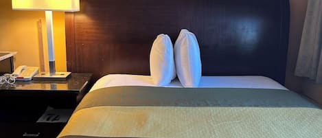 A hotel room with a bed, pillows, a nightstand with a lamp, and a telephone.