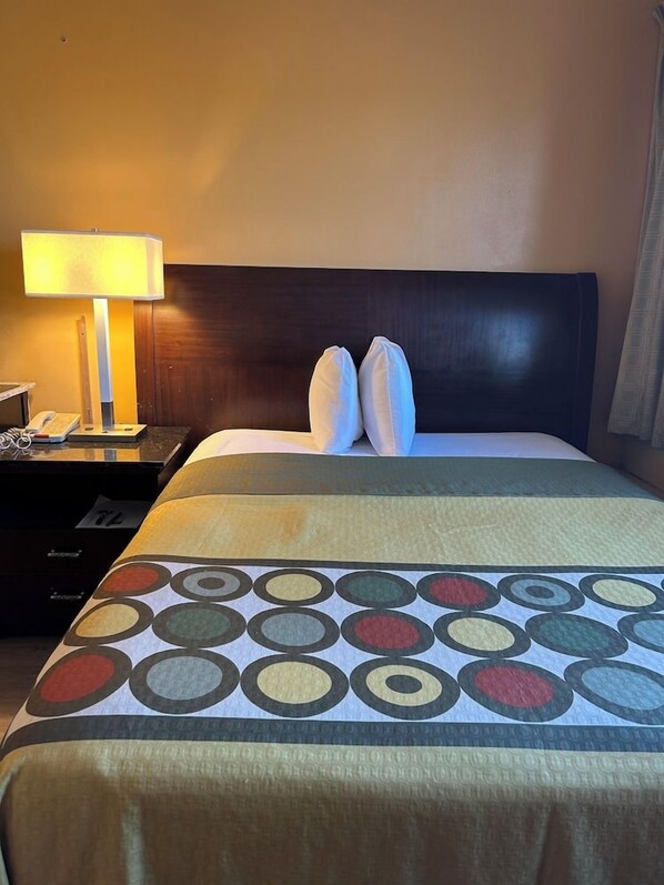 A hotel room with a bed, a nightstand with a lamp, and a telephone. - Traveler Inn Sterling (Sterling)