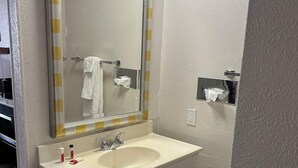 Un baño con un lavamanos blanco, un espejo con rayas amarillas y blancas, y un perchero para toallas.