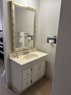 A bathroom with a white sink, a mirror with yellow and white stripes, and a towel rack. - Traveler Inn Sterling (Sterling)