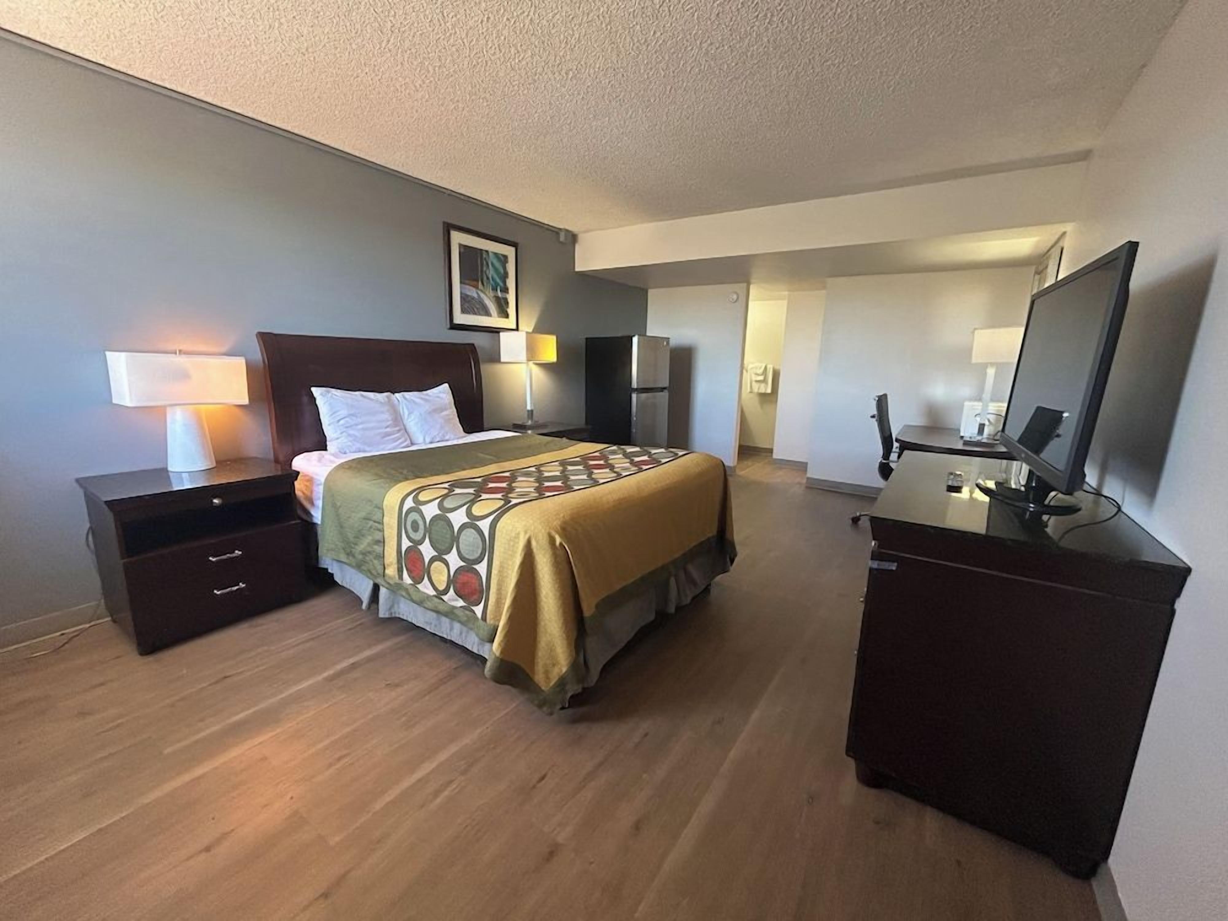 Ein Hotelzimmer mit Bett, Nachttischen, Schreibtisch, Stuhl, Fernseher und Kühlschrank.