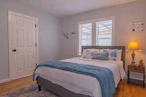 A bedroom with a bed, a nightstand, a lamp, a window, and a door. - Chic 4-bed with AC in beautiful Colorado Springs near downtown and pet friendly (Colorado Springs)