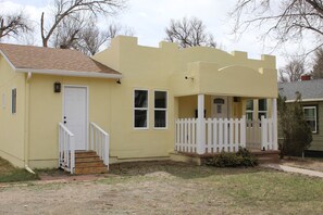 A single-story building with a white door, a small porch with a white picket fence, and a visible number on the side. - Chic 4-bed with AC in beautiful Colorado Springs near downtown and pet friendly (Colorado Springs)