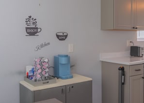 A kitchen with a wall decal that reads 'ENJOY LOVE' and 'Kitchen,' a coffee machine, a toaster, and a water dispenser on the counter. - Chic 4-bed with AC in beautiful Colorado Springs near downtown and pet friendly (Colorado Springs)