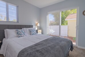A bedroom with a bed, a nightstand, a lamp, and a view of the outside. - Chic 4-bed with AC in beautiful Colorado Springs near downtown and pet friendly (Colorado Springs)