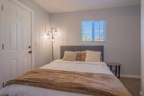 A bedroom with a bed, a nightstand, a window with blinds, and a door. - Chic 4-bed with AC in beautiful Colorado Springs near downtown and pet friendly (Colorado Springs)