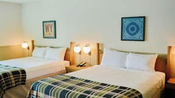 A hotel room with two beds, each with white linens and plaid blankets. There are wall-mounted lamps and a framed picture on the wall.