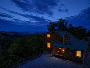 Eine zweistöckige Holzblockhütte mit Metall-Dach, umgeben von Bäumen und einer Schotterauffahrt.
