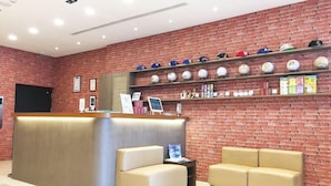 A reception area with a brick wall, a reception desk, two sofas, and shelves with hats and sports balls. - Kindness Hotel Lio He Ye Shi (Kaohsiung)